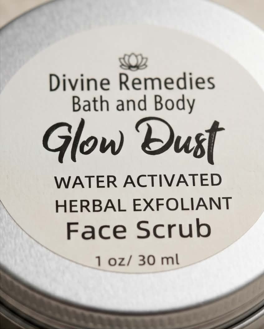 Close-up of a round silver metal tin lid with a cream-colored label reading 'Divine Remedies Bath and Body Glow Dust Water Activated Herbal Exfoliant Face Scrub 1 oz / 30 ml'.